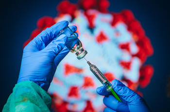 Eine Spritze und im Hintergrund ein Symbol des Coronavirus'