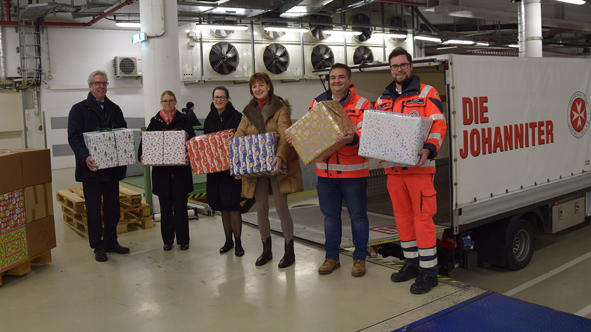 Sechs Personen halten Weihnachtsgeschenke in der Hand und stehen vor einem kleinen LKW