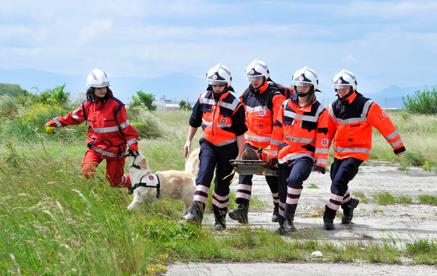 Vier Johanniter tragen eine verletzte Perosn auf einer Trage. Daneben ist eine Johanniterin mit ihrem Rettungshund.