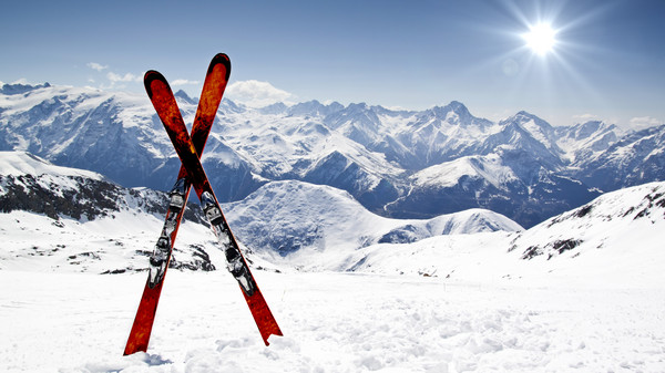 zwei gekreuzte rote Schi stecken im Schnee, im Hintergrund sieht man verschneite Berge