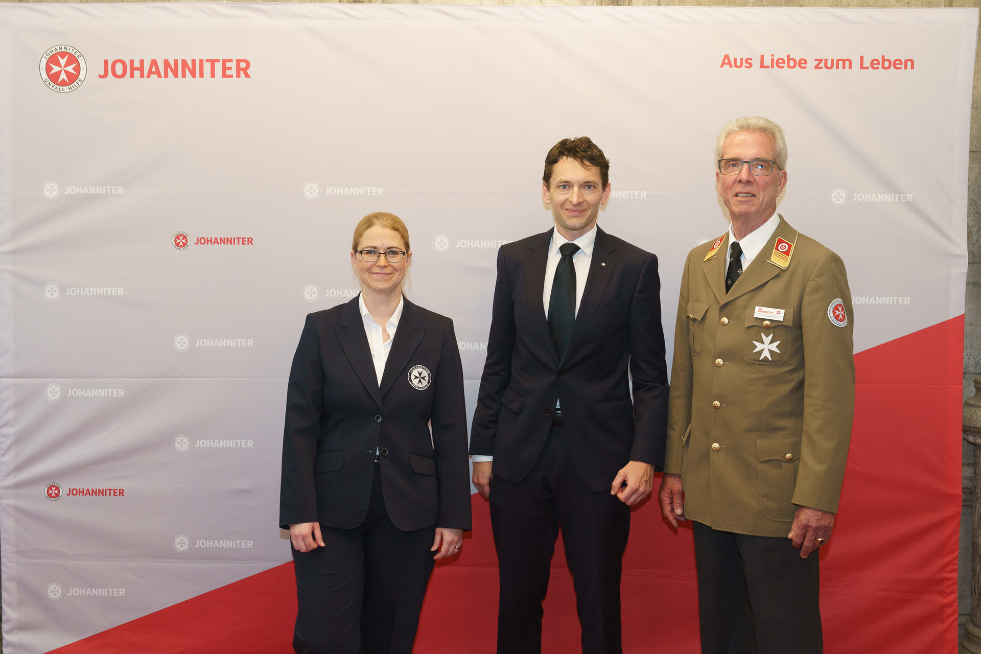 Präsident Johannes Bucher und Bundesgeschäftsführerin Petra Grell-Kunzinger mit Personen vor einer Johanniter Leinwand