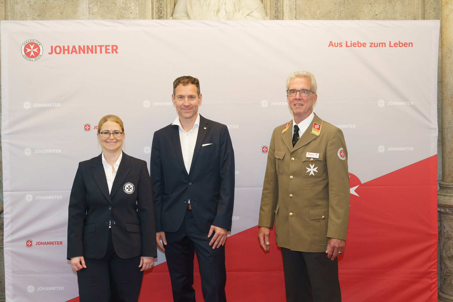 Präsident Johannes Bucher und Bundesgeschäftsführerin Petra Grell-Kunzinger mit Personen vor einer Johanniter Leinwand