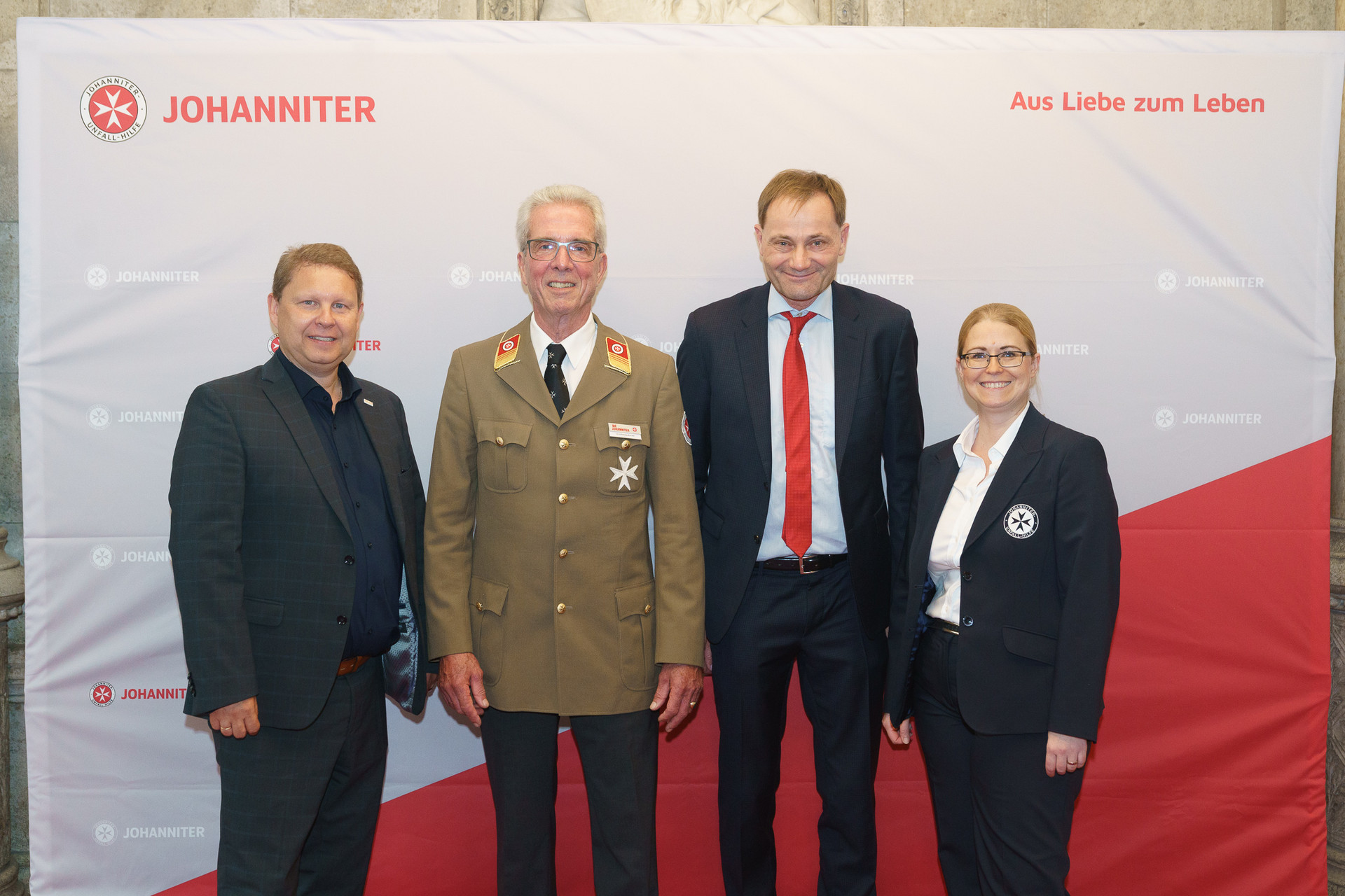 Präsident Johannes Bucher und Bundesgeschäftsführerin Petra Grell-Kunzinger mit Personen vor einer Johanniter Leinwand
