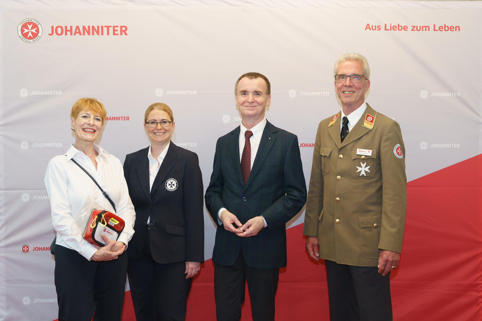 Präsident Johannes Bucher und Bundesgeschäftsführerin Petra Grell-Kunzinger mit Personen vor einer Johanniter Leinwand