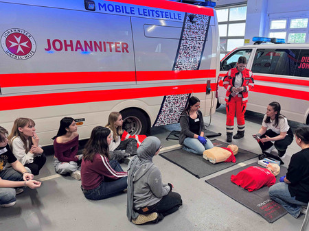 Jungen Mädchen wird die Reanimation anhand von Übungspuppen erklärt.
