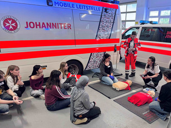 Jungen Mädchen wird die Reanimation anhand von Übungspuppen erklärt.