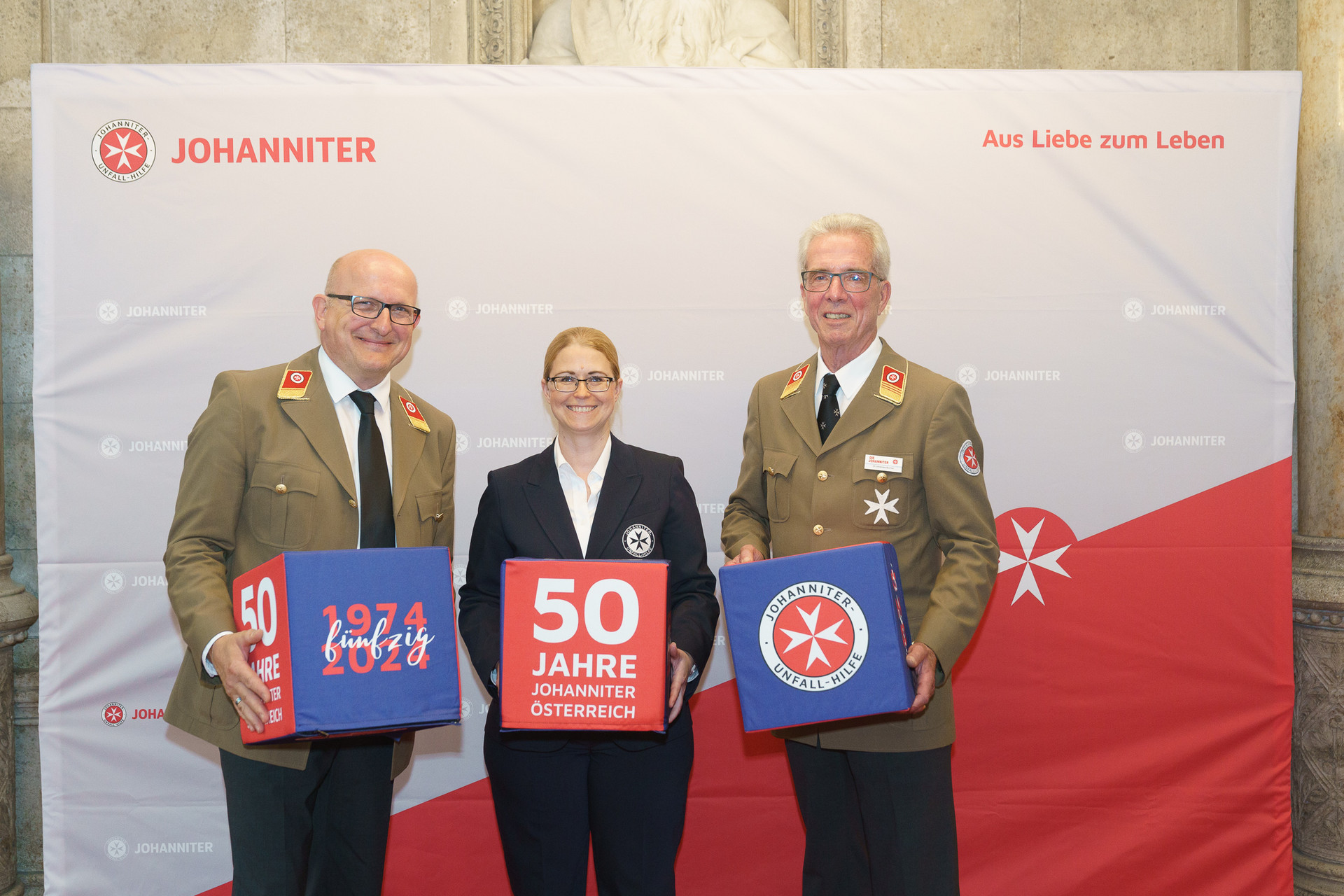 Präsident Johannes Bucher und Bundesgeschäftsführerin Petra Grell-Kunzinger mit Personen vor einer Johanniter Leinwand
