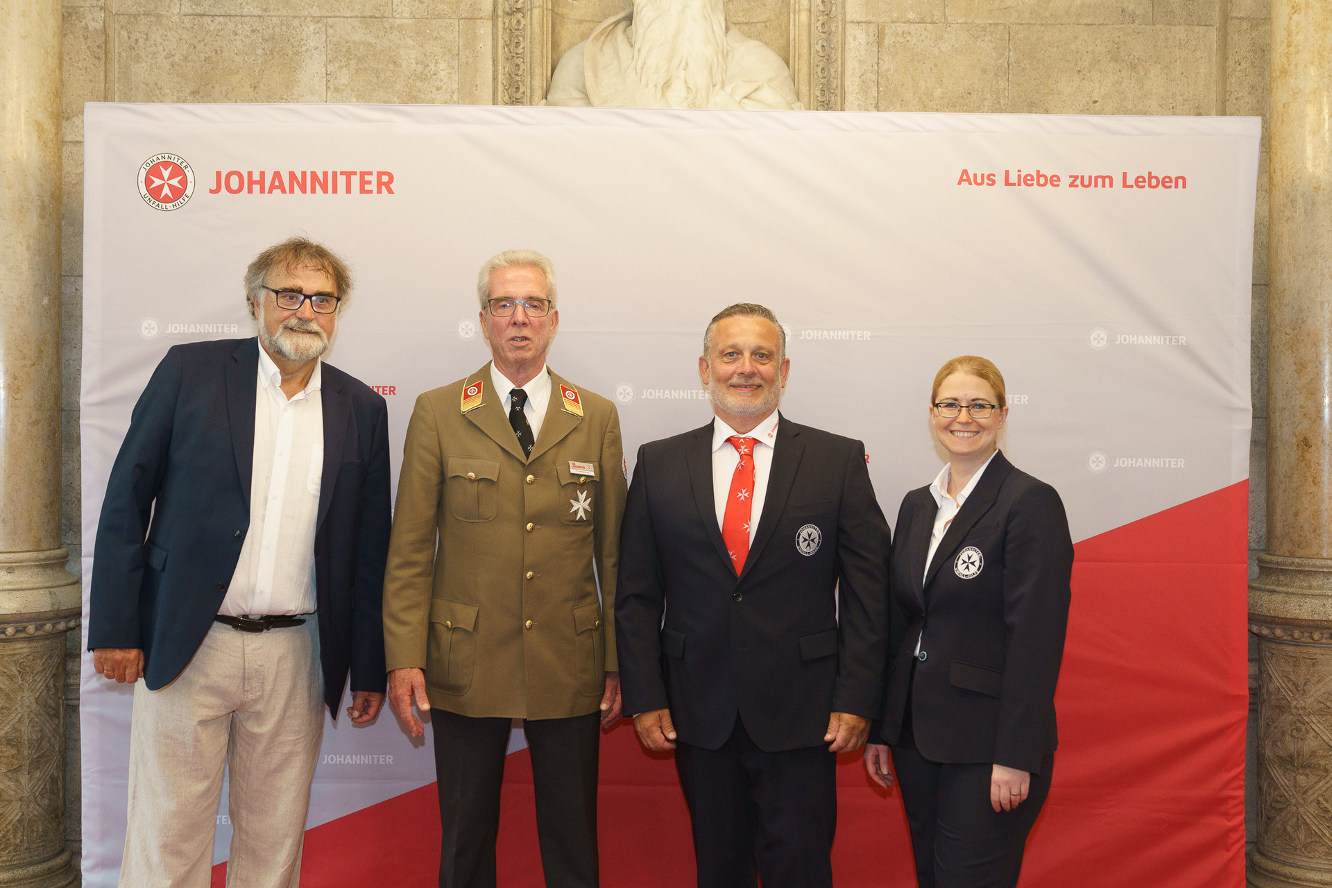 Präsident Johannes Bucher und Bundesgeschäftsführerin Petra Grell-Kunzinger mit Personen vor einer Johanniter Leinwand