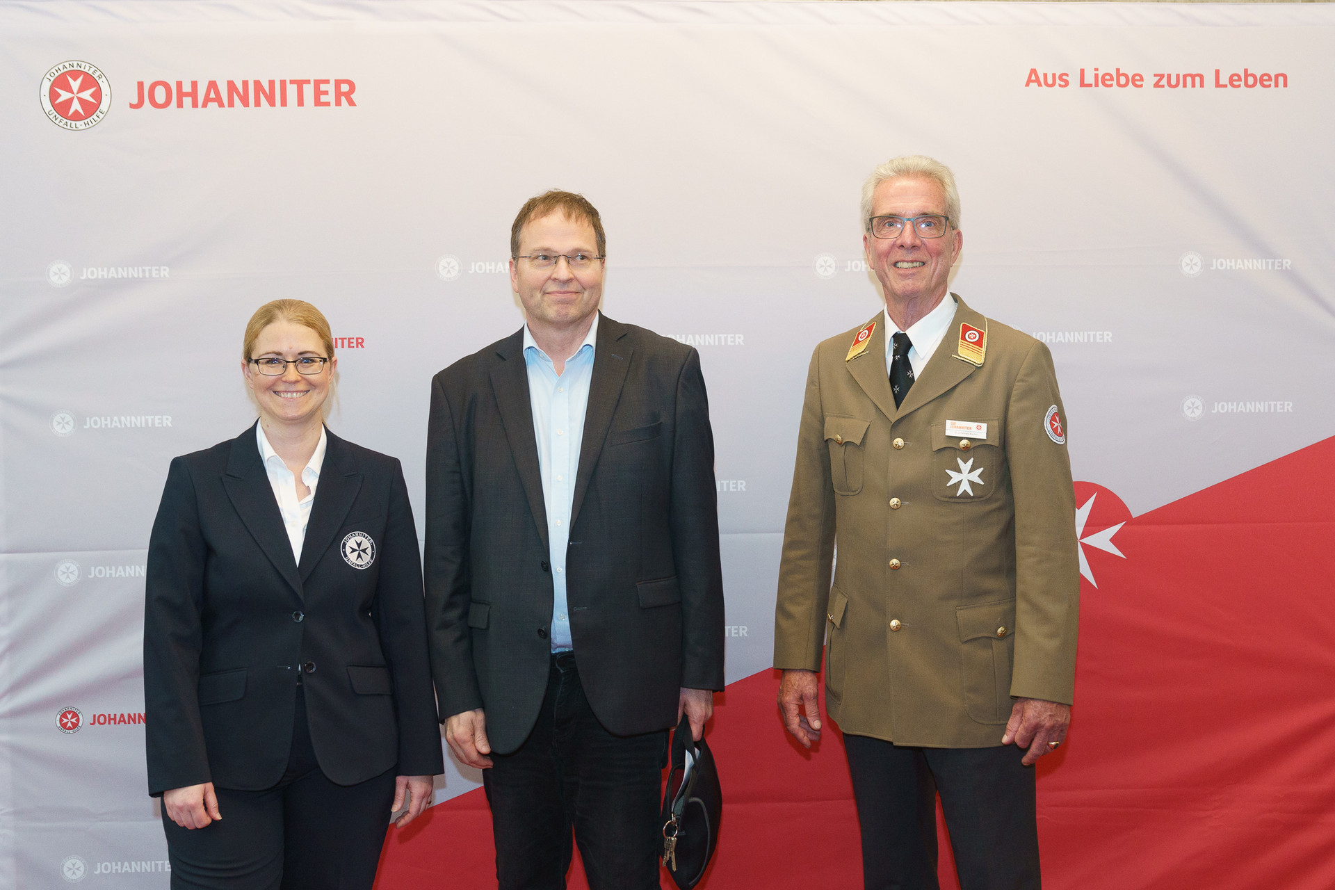Präsident Johannes Bucher und Bundesgeschäftsführerin Petra Grell-Kunzinger mit Personen vor einer Johanniter Leinwand