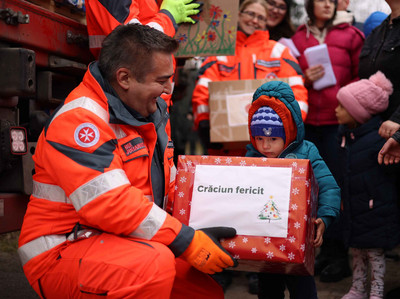 Ein Johanniter übergibt einem Kind das Paket des Weihnachtstruckers.
