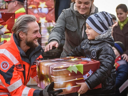 Ein Johanniter übergibt einem kleinen Jungen ein Geschenkspaket vom Weihnachtstrucker.