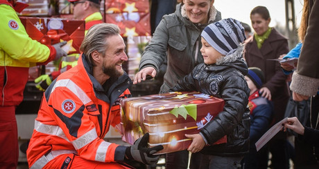 Ein Johanniter übergibt einem kleinen Jungen ein Geschenkspaket vom Weihnachtstrucker.