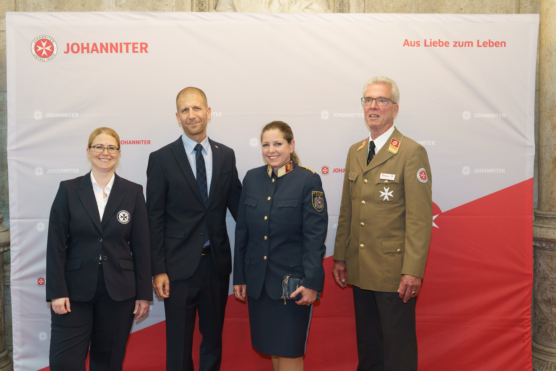 Präsident Johannes Bucher und Bundesgeschäftsführerin Petra Grell-Kunzinger mit Personen vor einer Johanniter Leinwand