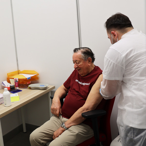 Arzt verabreicht einem sitzenden Patienten eine Spritze