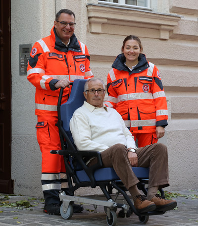 Zwei Johanniter:innen holen einen Fahrdienst-Klient mit einem Tragsessel von zu Hause ab.