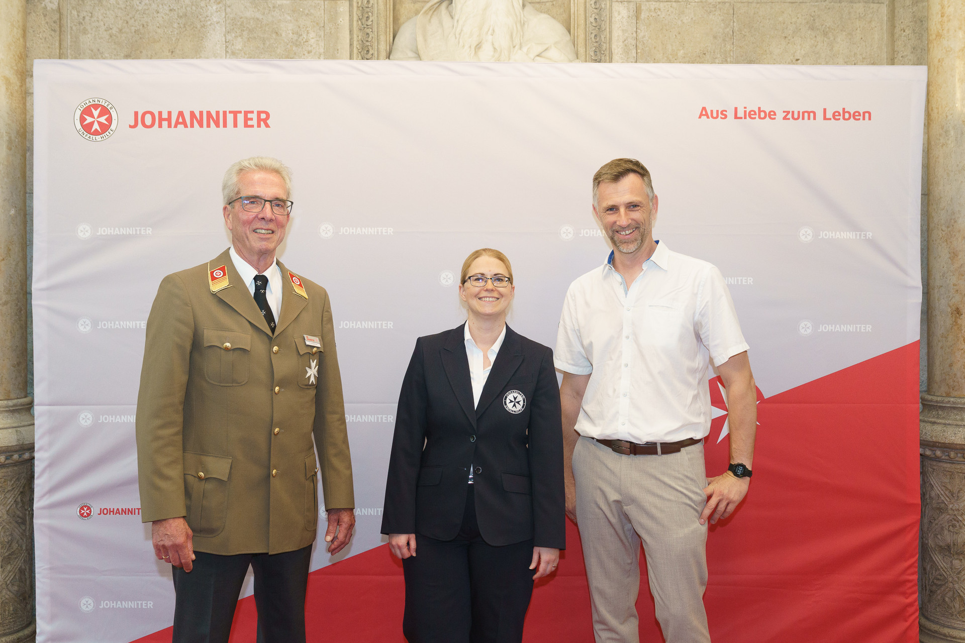 Präsident Johannes Bucher und Bundesgeschäftsführerin Petra Grell-Kunzinger mit Personen vor einer Johanniter Leinwand
