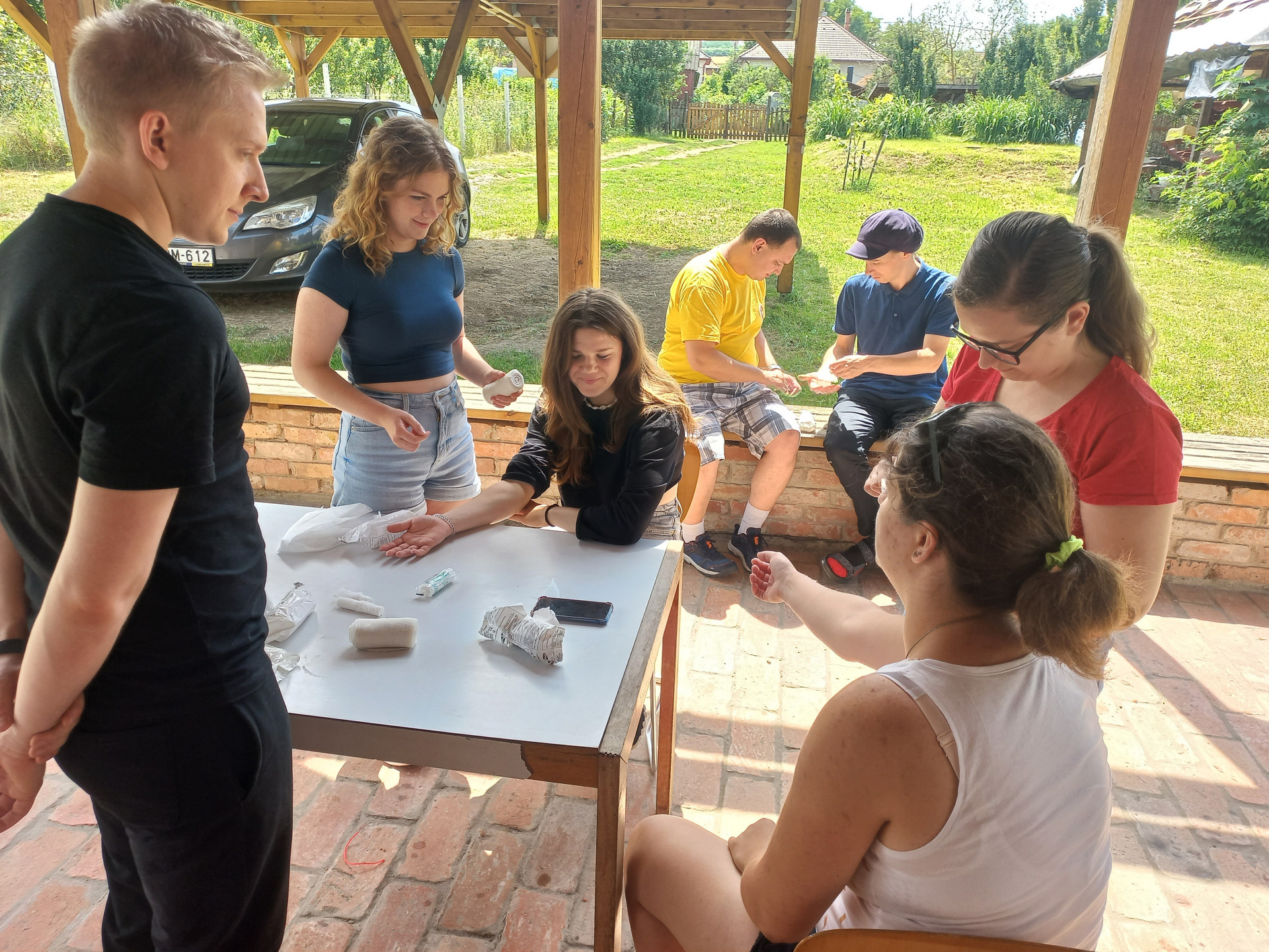mehrere Personen sitzen um einen Tisch und üben das Anlegen von Verbänden