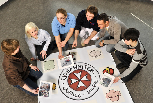 Ein Kursleiter und fünf Kursteilnehmende beim interaktiven Erste-Hilfe-Unterricht