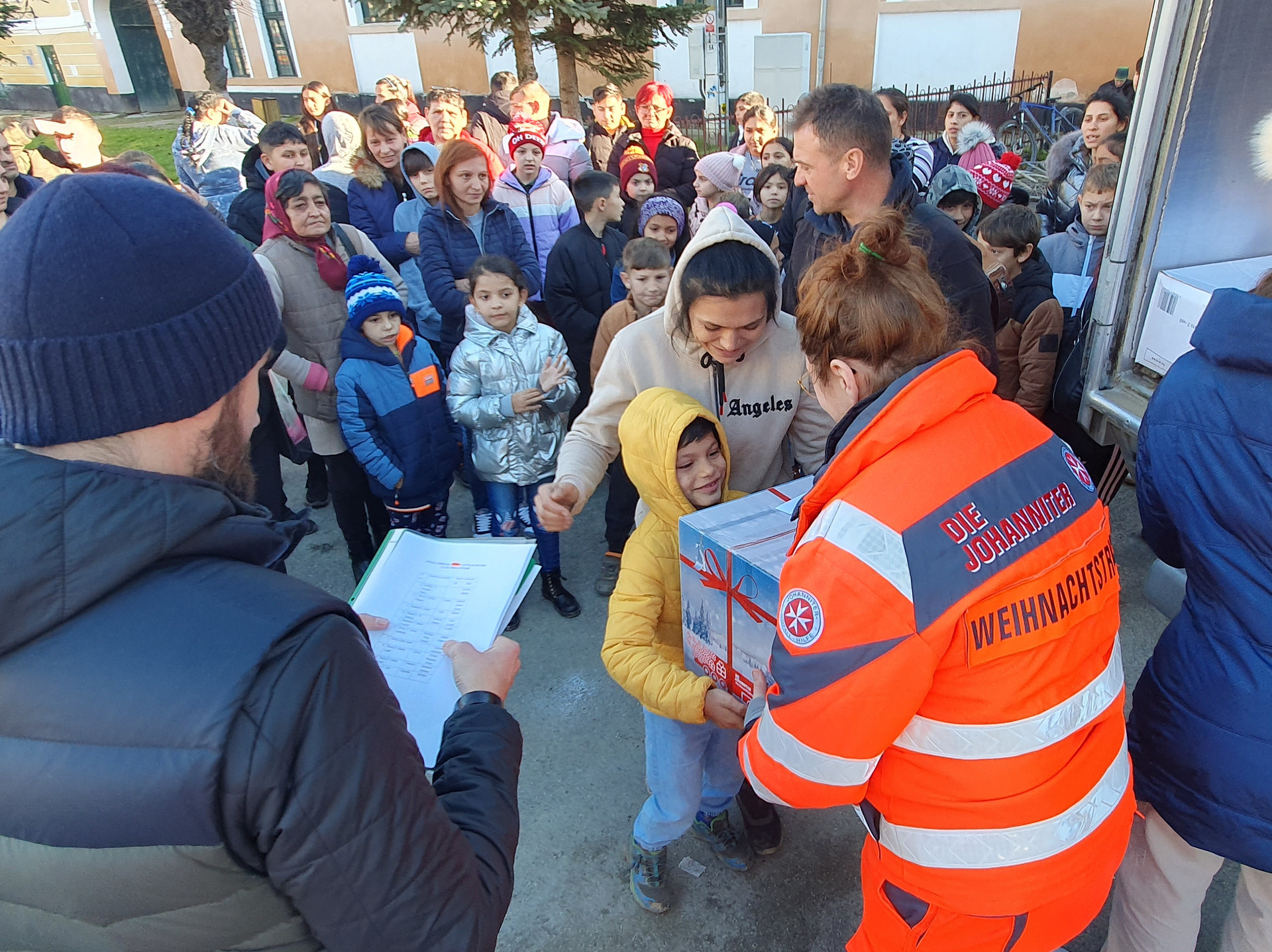 Eine Johanniterin übergibt einem Jungen ein Weihnachtstrucker-Paket.