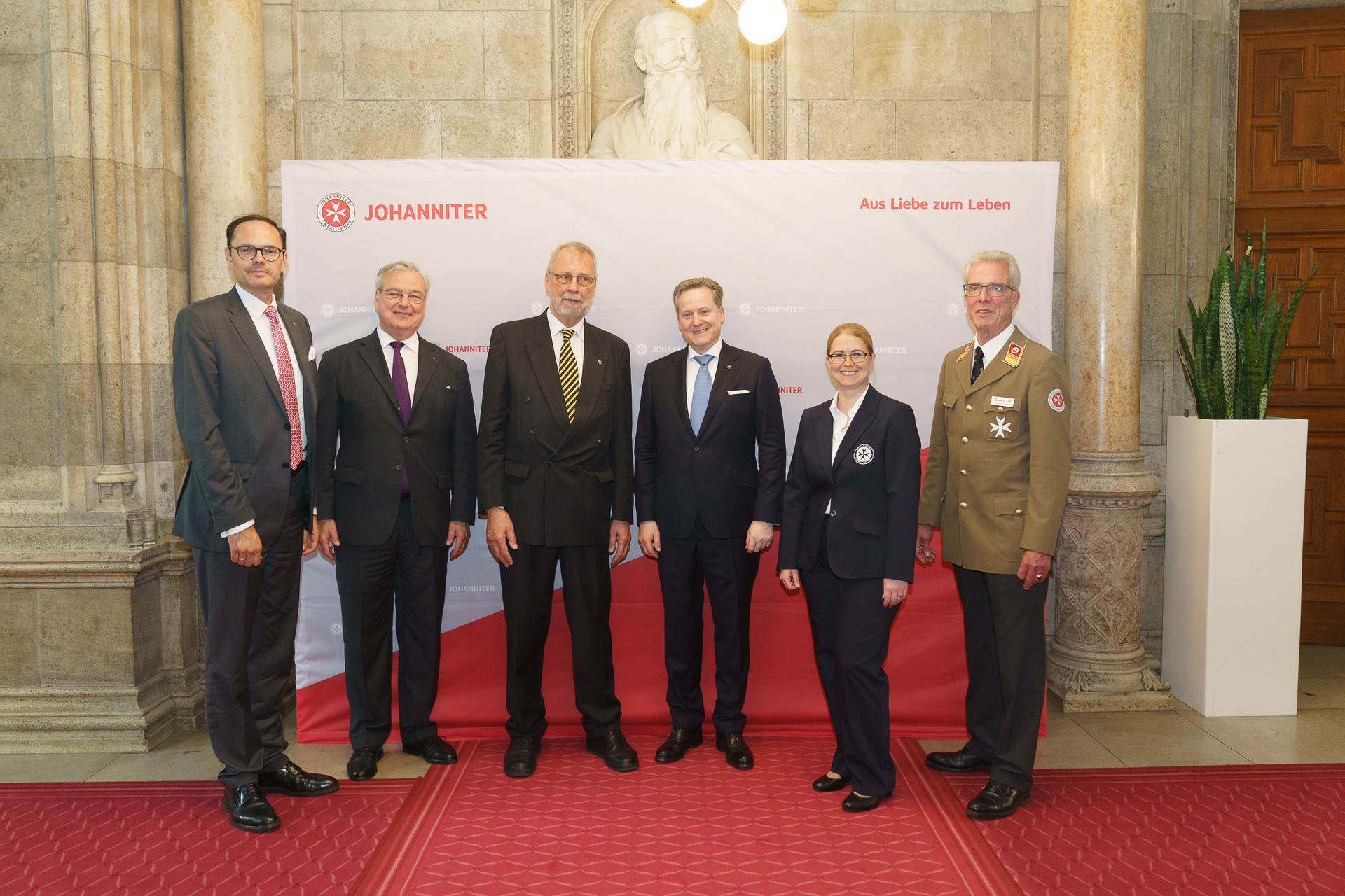 Präsident Johannes Bucher und Bundesgeschäftsführerin Petra Grell-Kunzinger mit Personen vor einer Johanniter Leinwand