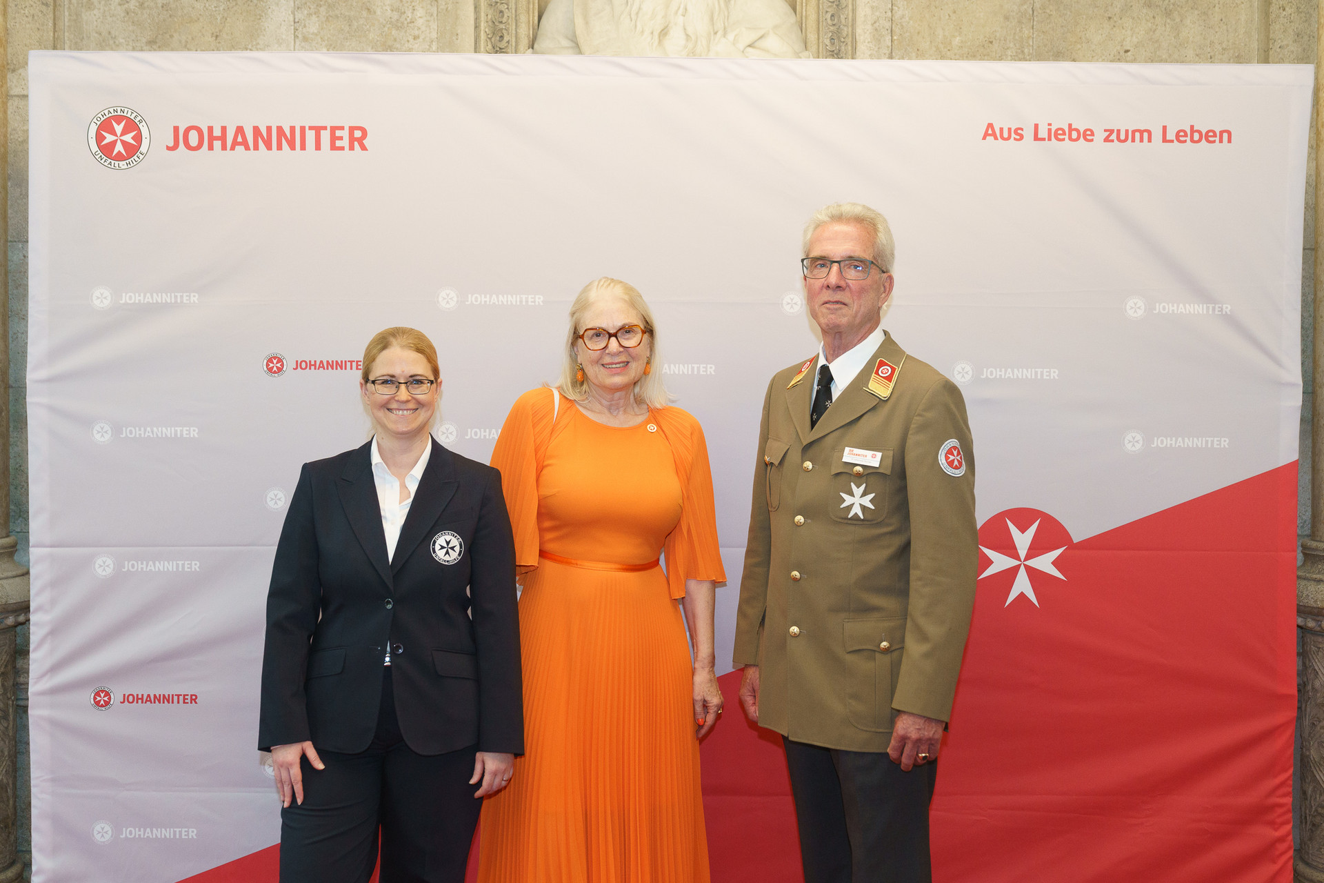 Präsident Johannes Bucher und Bundesgeschäftsführerin Petra Grell-Kunzinger mit Personen vor einer Johanniter Leinwand