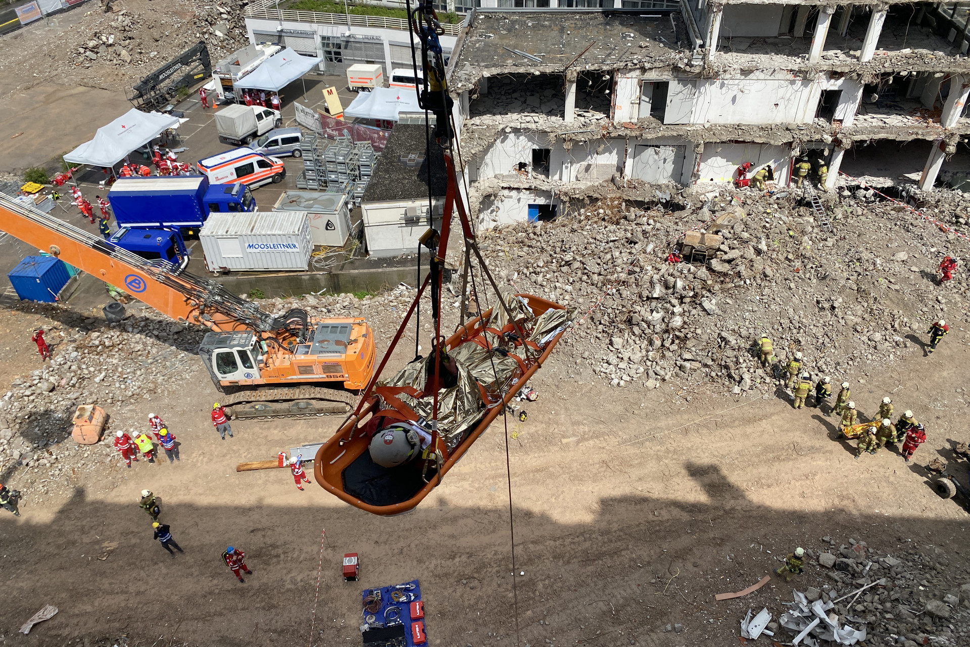 Eine Trage hängt an einem Kran und schwebt über einem abgerissenen Gebäude