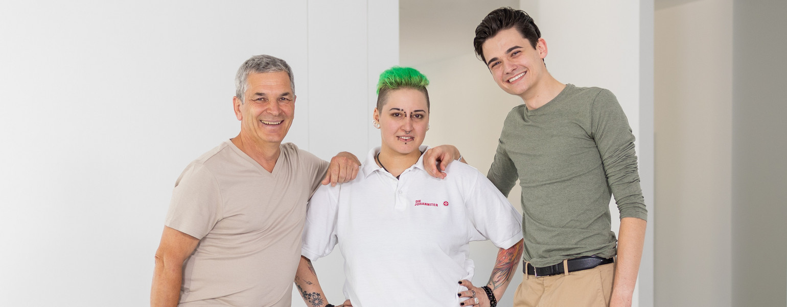 Ein älterer und ein jüngerer Mann lehnen sich rechts und links an der Schulter einer Johanniterin an.