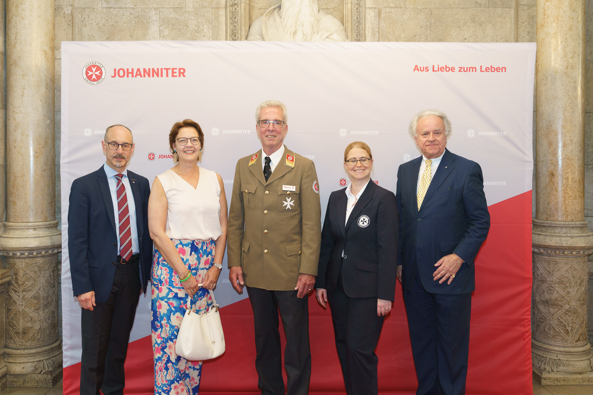 Präsident Johannes Bucher und Bundesgeschäftsführerin Petra Grell-Kunzinger mit Personen vor einer Johanniter Leinwand