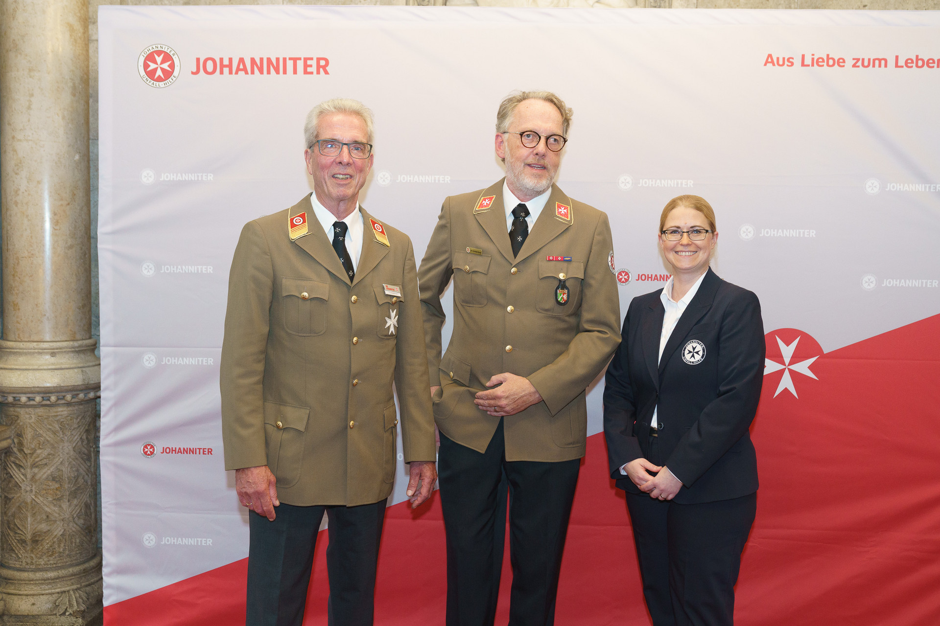 Präsident Johannes Bucher und Bundesgeschäftsführerin Petra Grell-Kunzinger mit Personen vor einer Johanniter Leinwand
