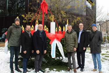 Angehörige der Diakonie übergeben draußen den Riesen-Adventkranz.