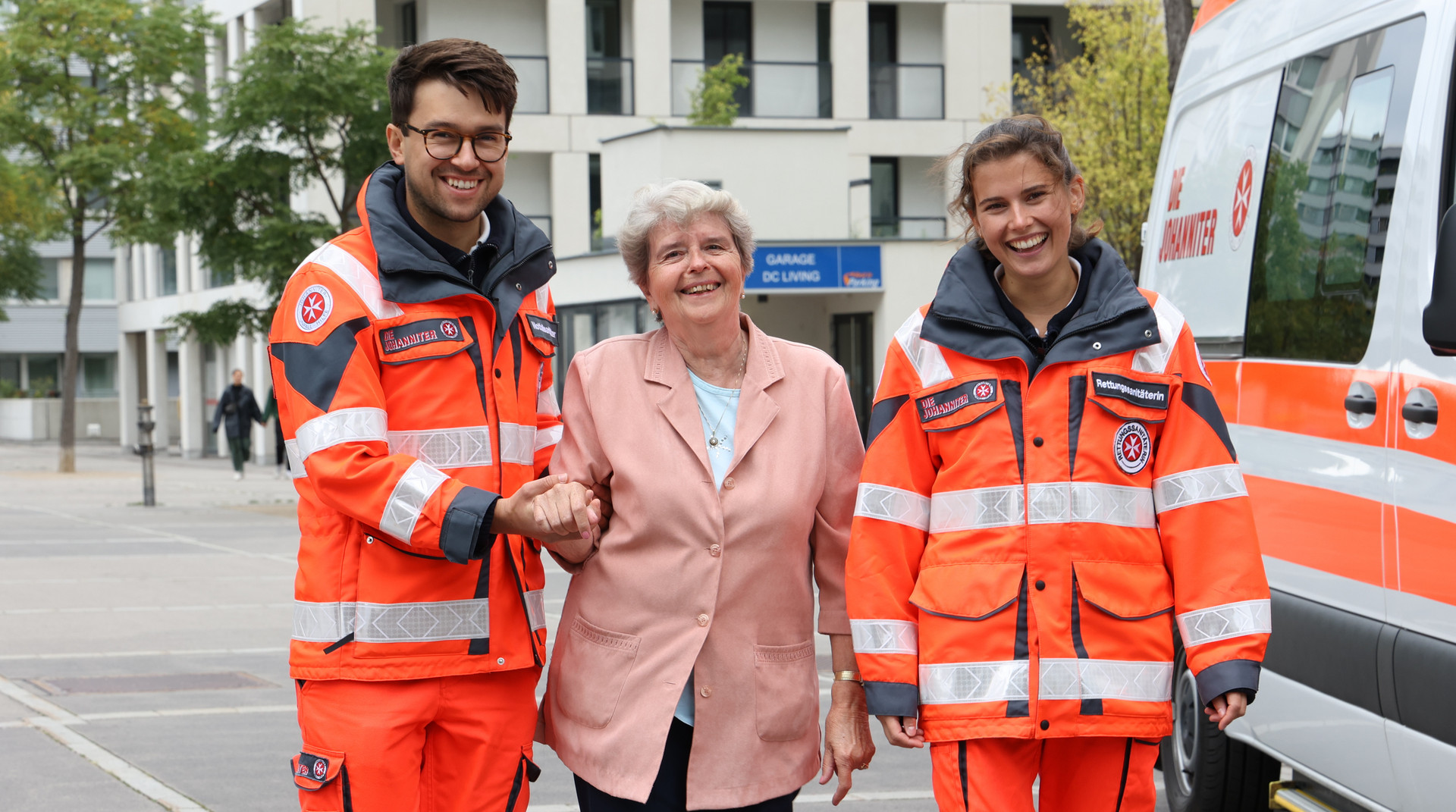 Zwei ehrenamtliche Rettungssanitäter:innen stützen eine Patientin beim Gehen.