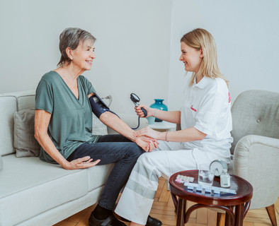Eine Pflegerin sitzt gegenüber von ihrer Patientin und misst den Blutdruck.