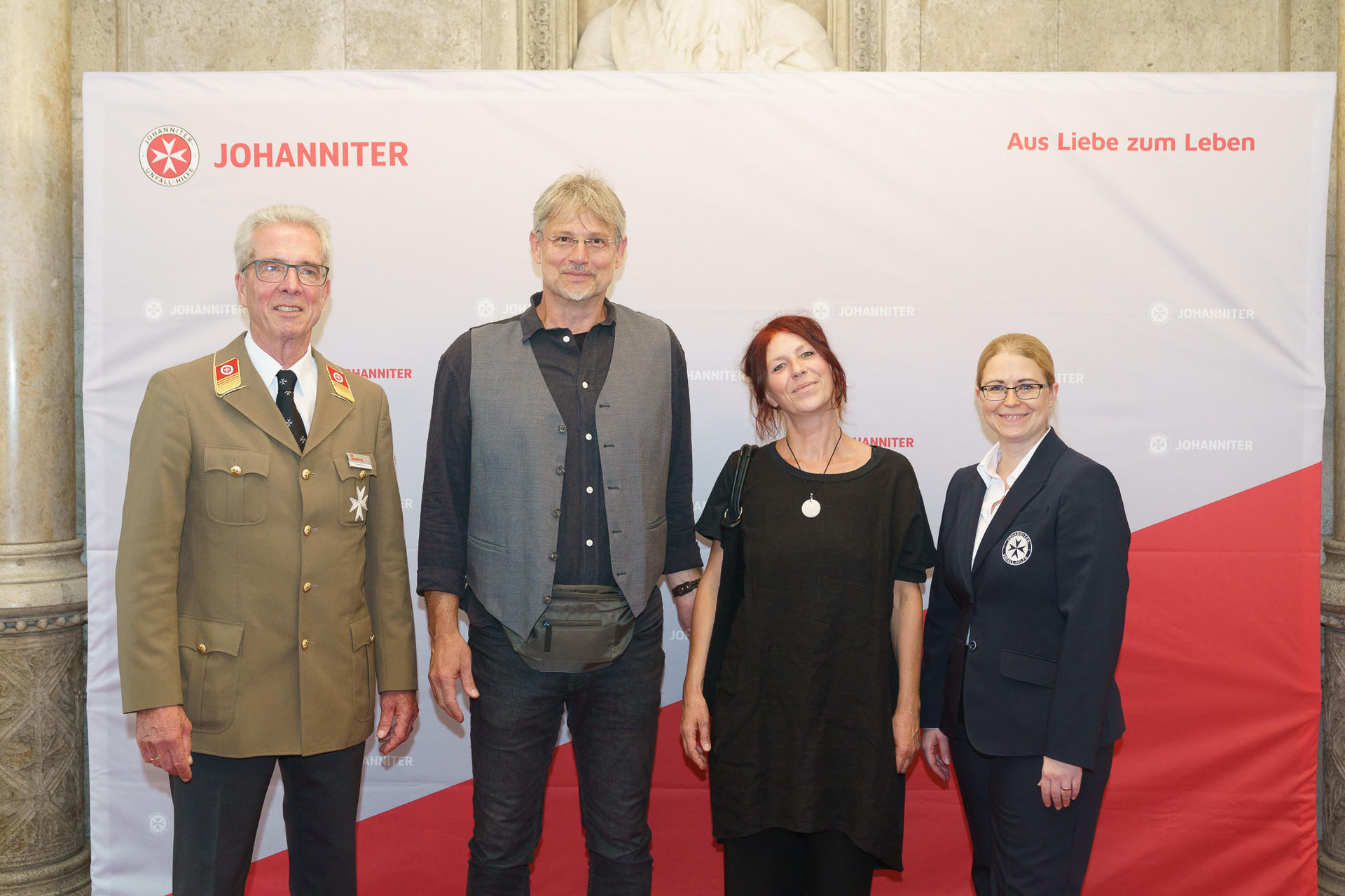 Präsident Johannes Bucher und Bundesgeschäftsführerin Petra Grell-Kunzinger mit Personen vor einer Johanniter Leinwand