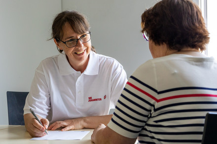 Die Community Nurse schreibt bei einem Beratungsgespräch wichtige Dinge für die Klientin auf einem Schreibblock mit.