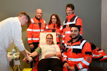 4 Johanniter:innen stehen um eine Liege, wo der Kollegin gerade Blut abgenommen wird.