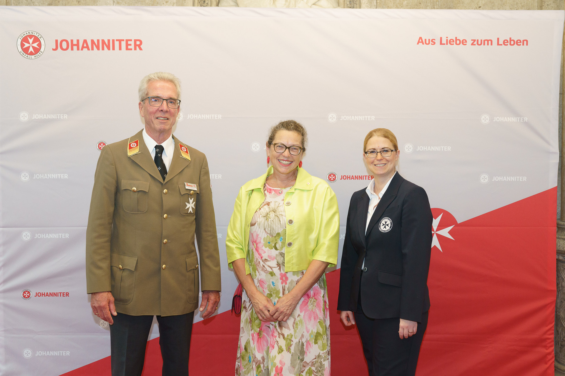 Präsident Johannes Bucher und Bundesgeschäftsführerin Petra Grell-Kunzinger mit Personen vor einer Johanniter Leinwand