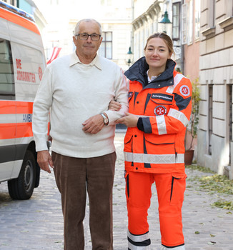 Eine Johanniterin vom Fahrdienst unterstützt einen Patienten beim Gehen.