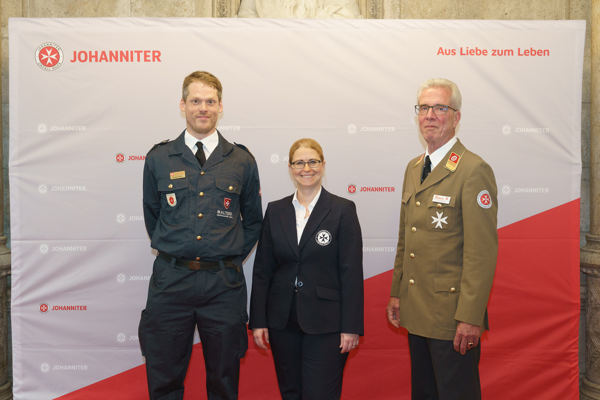 Präsident Johannes Bucher und Bundesgeschäftsführerin Petra Grell-Kunzinger mit Personen vor einer Johanniter Leinwand