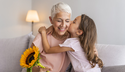 Ein Mädchen gibt ihrer Oma einen Kuss auf die Wange und umarmt sie dabei.