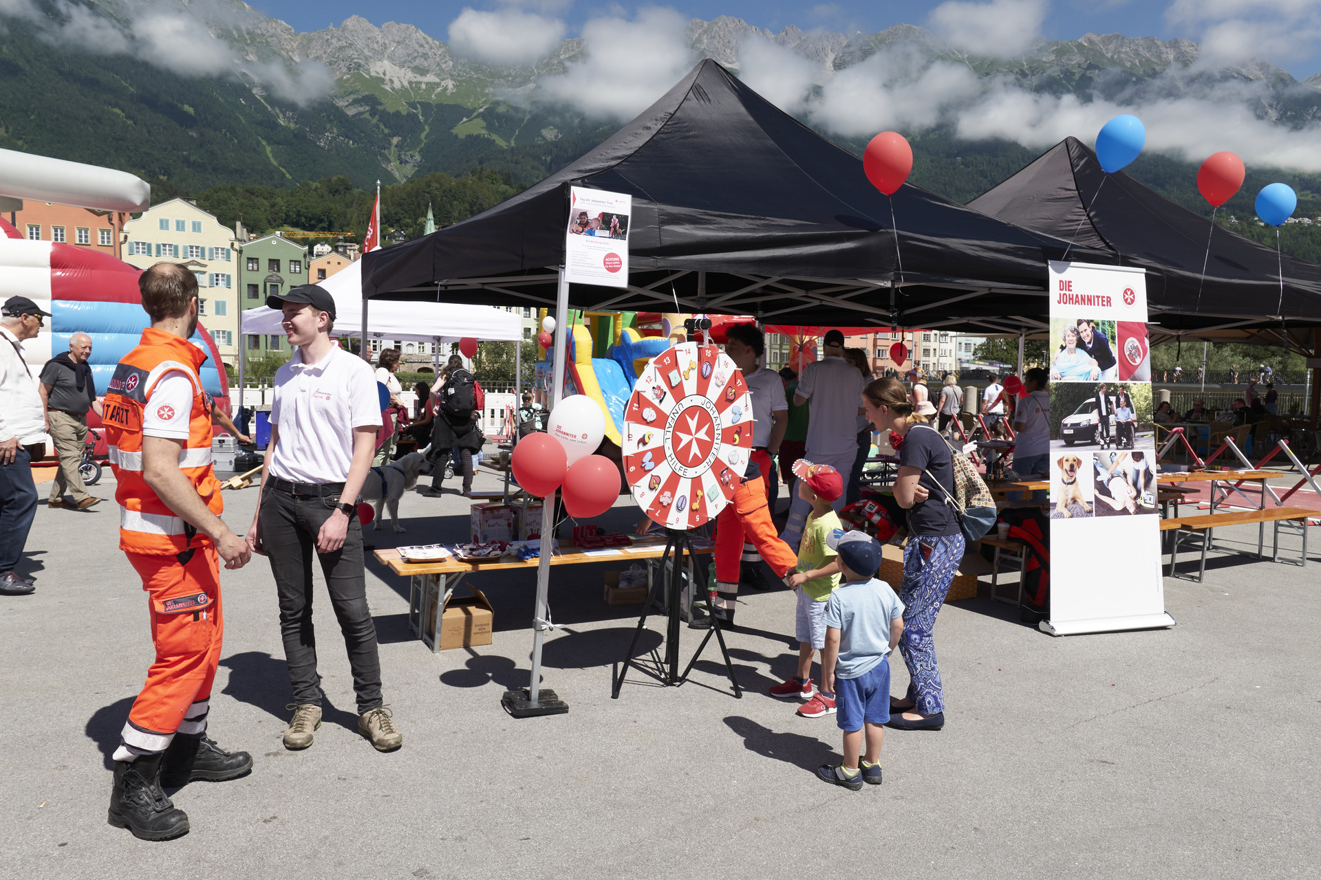 Vor den Zelten steht ein Glücksrad zum Thema Erste Hilfe. Davor stehen zwei Buben und eine Frau, die das Rad anschauen.