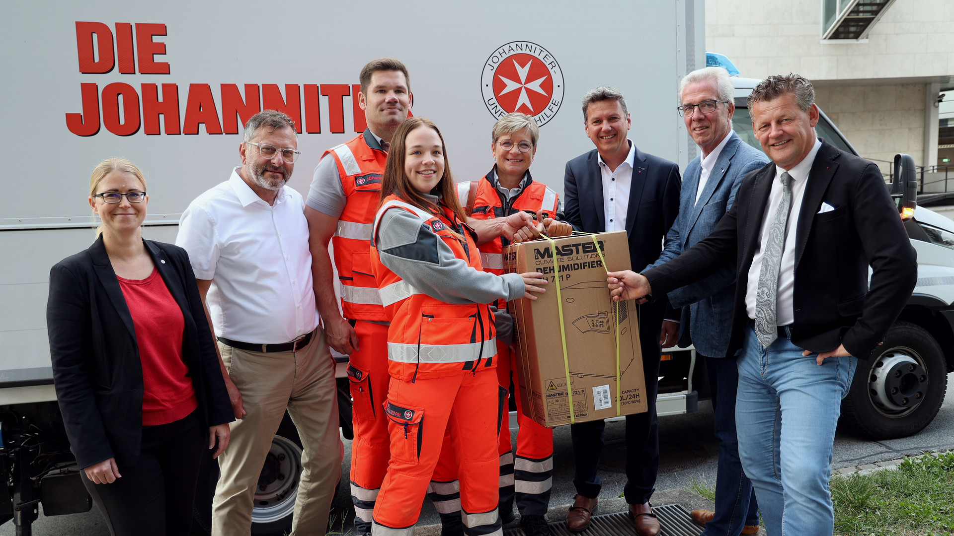 mehrere Personen possieren vor einem LKW, die Personen in der Mitte halten einen Karton mit einem Trocknungsgerät hochn