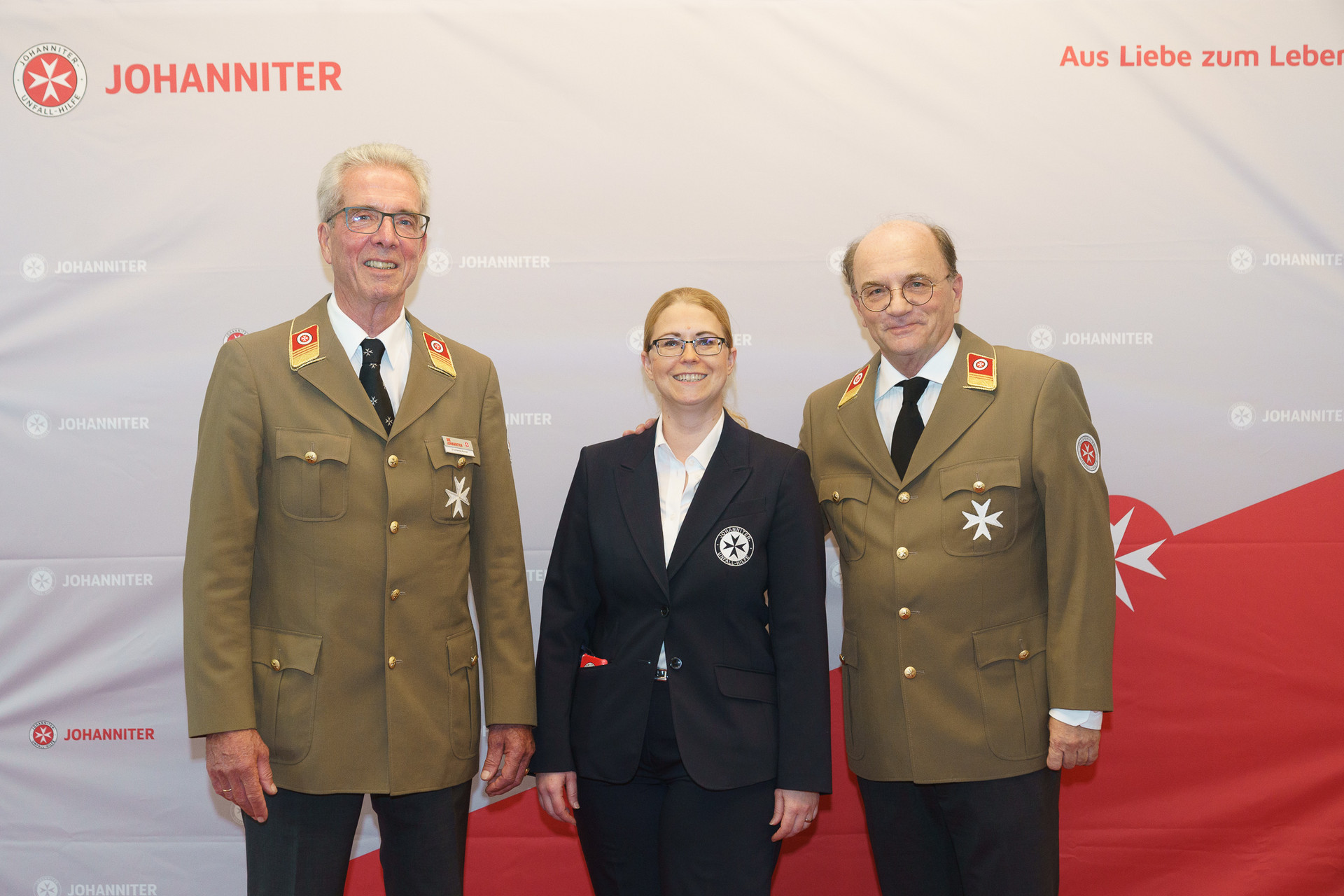 Präsident Johannes Bucher und Bundesgeschäftsführerin Petra Grell-Kunzinger mit Personen vor einer Johanniter Leinwand