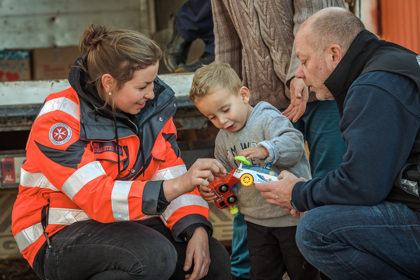 Eine Rettungssanitäterin überreicht einem Kind und einem Mann ein Paket