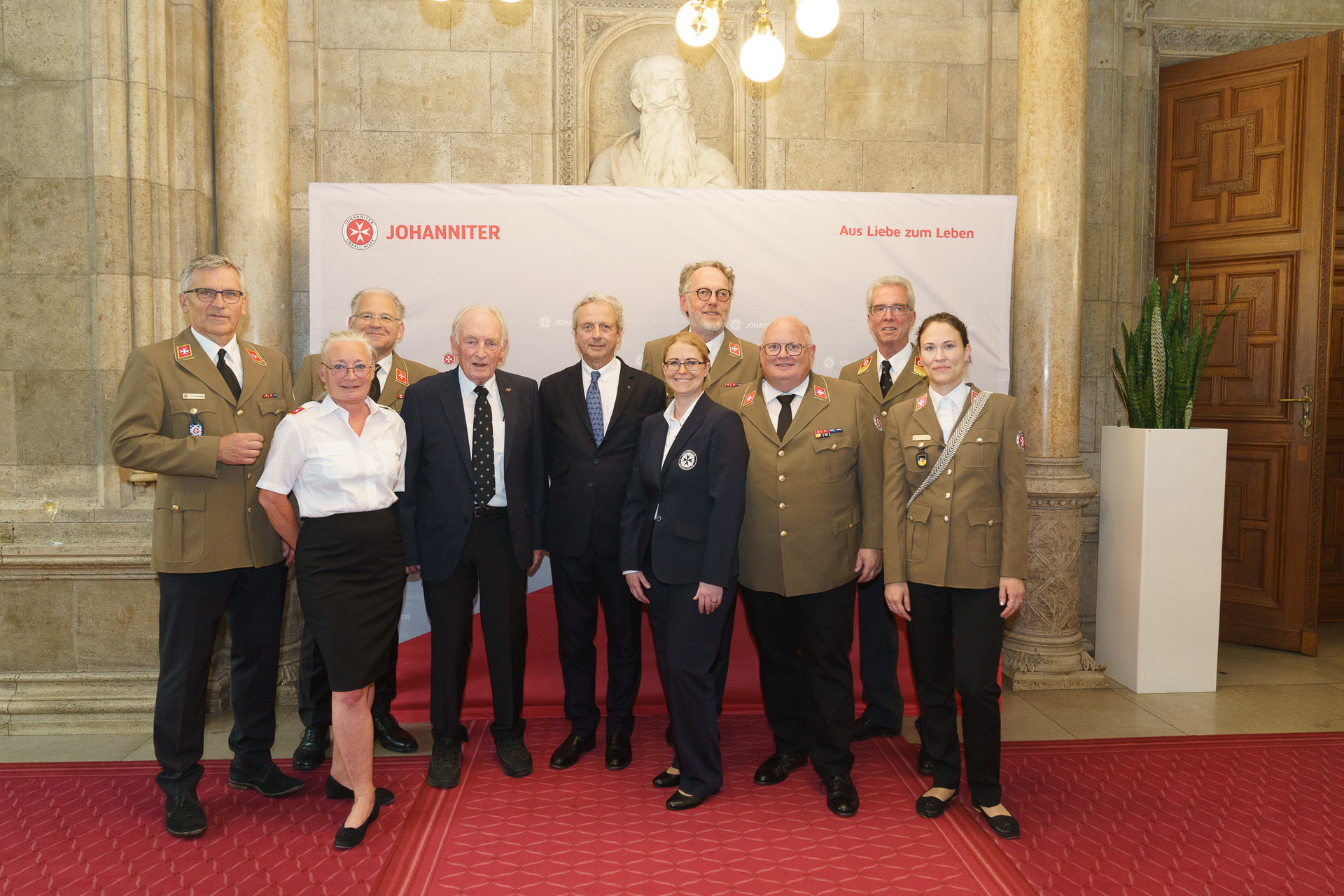 Präsident Johannes Bucher und Bundesgeschäftsführerin Petra Grell-Kunzinger mit Personen vor einer Johanniter Leinwand