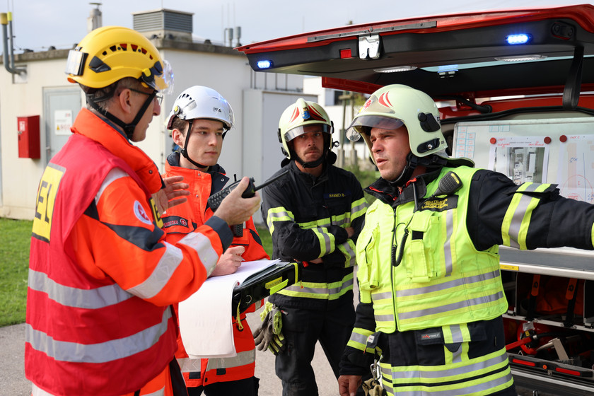 Der Einsatzleiter redet mit einem Sanitäter und zwei Feuerwehrmännern um den Einsatz zu koordinieren.