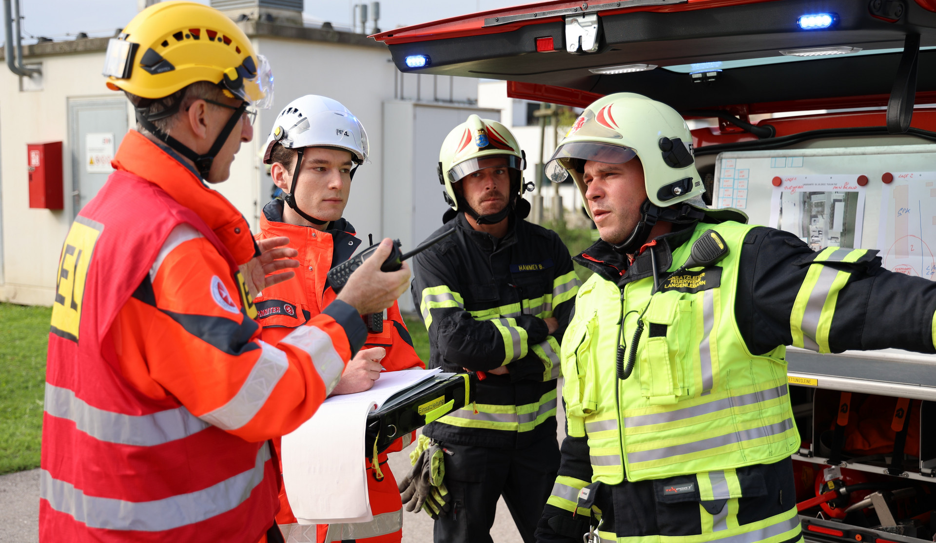 Der Einsatzleiter redet mit einem Sanitäter und zwei Feuerwehrmännern um den Einsatz zu koordinieren.