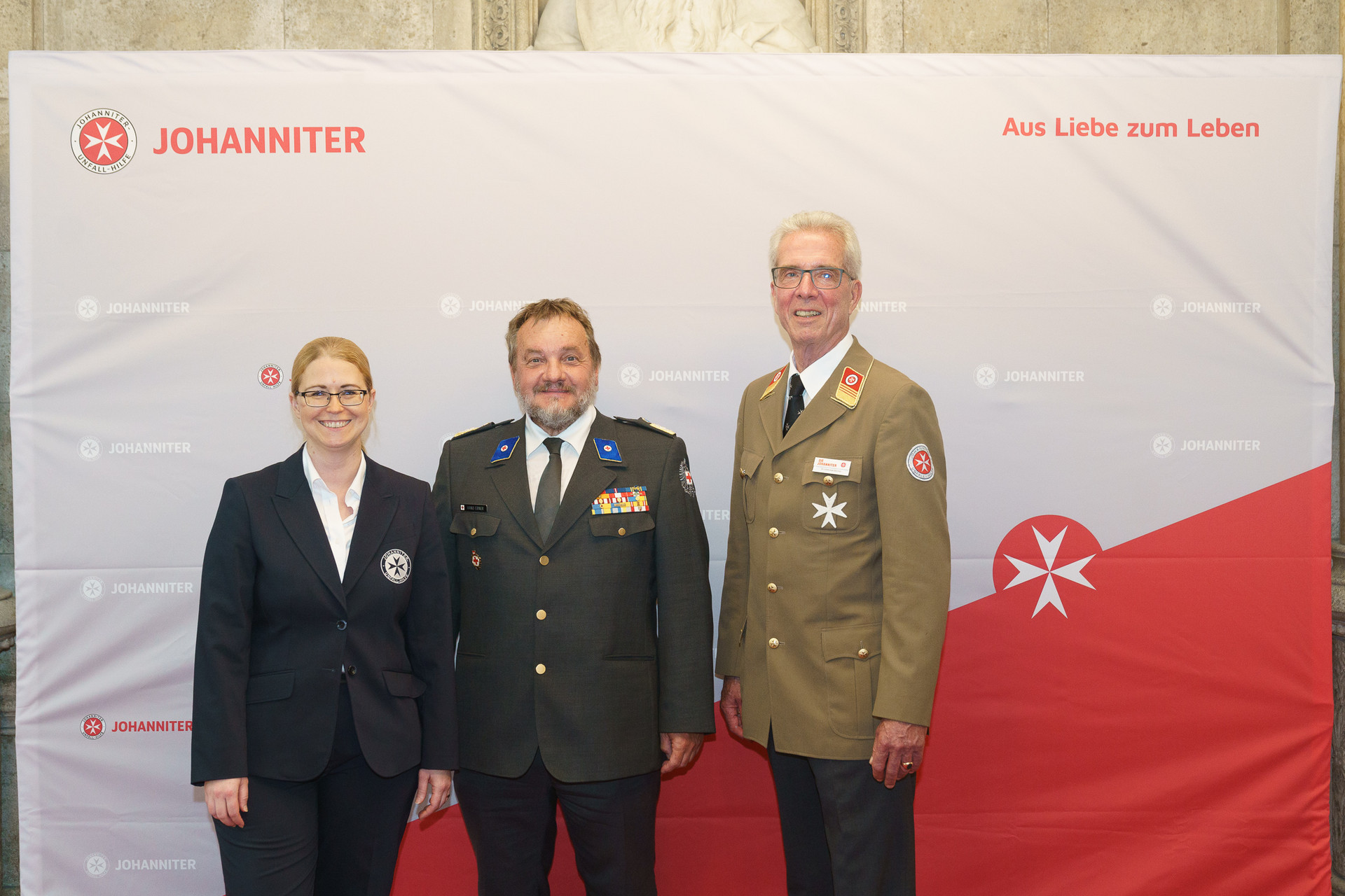 Präsident Johannes Bucher und Bundesgeschäftsführerin Petra Grell-Kunzinger mit Personen vor einer Johanniter Leinwand