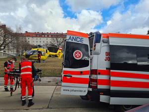 Zwei Sanitäter laden die Trage aus dem Auto aus. Im Hintergrund steht der Rettungshubschrauber.