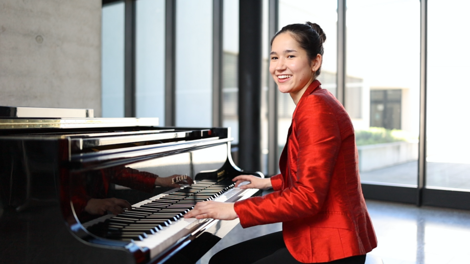 Eine Frau, Laetitia, spielt an einem Klavier und lacht in die Kamera.