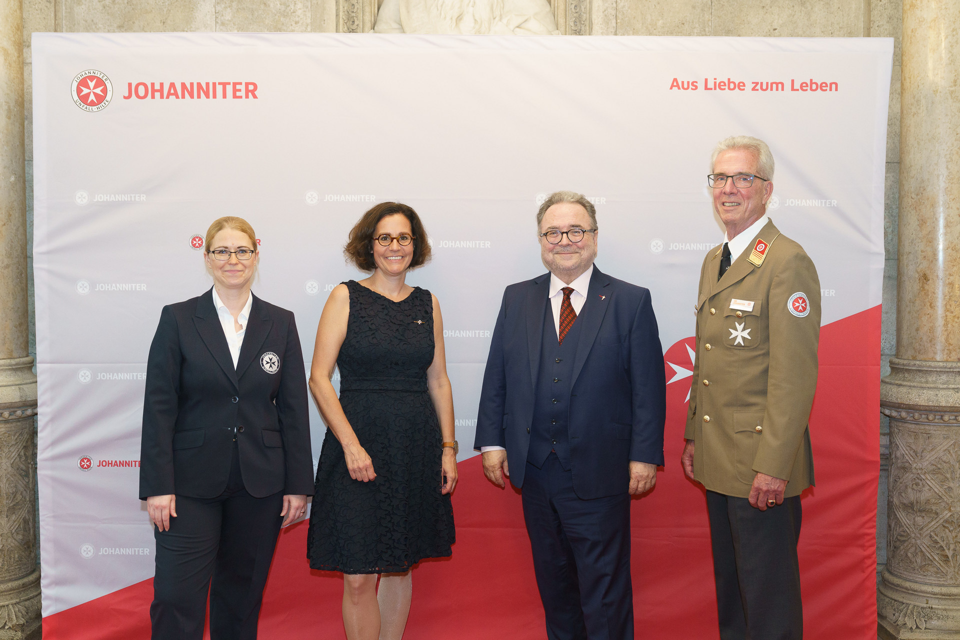 Präsident Johannes Bucher und Bundesgeschäftsführerin Petra Grell-Kunzinger mit Personen vor einer Johanniter Leinwand